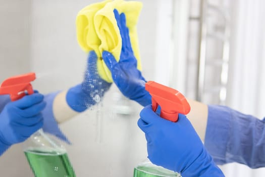 girl washing mirror with yellow cloth in blue gloves at home.House cleaning concept