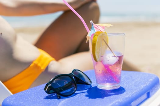 a sexy girl takes a pink cocktail close-up on the beach, a girl in a swimsuit lies on a sun lounger near the pool, close-up.The concept of relaxing on the beach. High quality photo