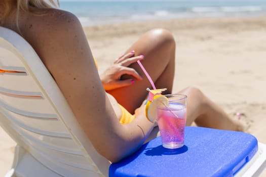 A woman in a swimsuit sits in a sun lounger with a glass of cocktail back view, a beautiful seascape has a place for an inscription. High quality photo