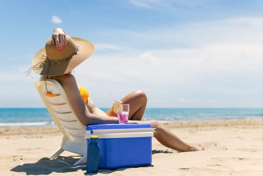 A sexy blonde in a bright bikini is sunbathing on a sun lounger with a cocktail in her hand by the sea. A beautiful girl is enjoying her summer holidays at an expensive resort, High quality photo