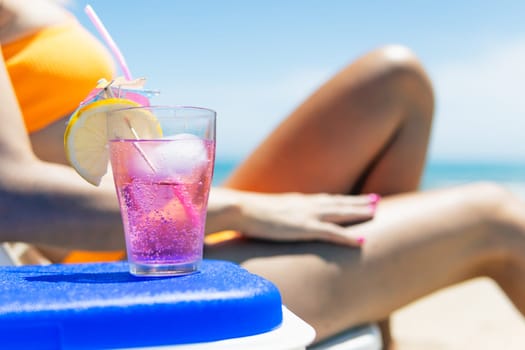 a pink cocktail close-up on the beach, a girl in a swimsuit lies on a sun lounger next to it stands a close-up of a pink color cocktail. The concept of relaxing on the beach. High quality photo