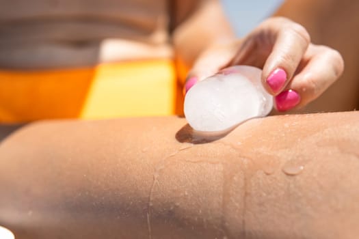 the girl on the beach is cooled by ice, close-up on the girl's leg and arm. High quality photo