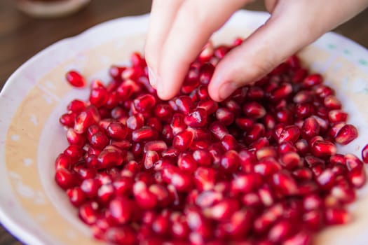 child's hand takes a red pomegranate from a plate close-up. High quality photo