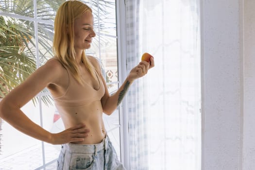 a happy, slender girl of European appearance stands in a house in big jeans and underwear and shows the result of losing weight and proper nutrition. she holds an apple in her hand. High quality photo