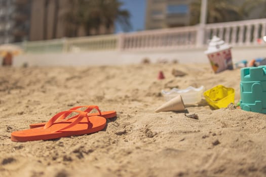 the beach landscape is beautiful, Bright plastic children's toys in the sand are orange flip-flops nearby. The concept of a beach holiday for children. Space for text.space for copy.High quality photo