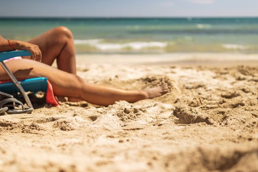 legs of a woman on the beach close-up, a woman sunbathes on a sunbed in a sitting position on the beach, near the sea, there is a place for an inscription. The concept of summer High quality photo