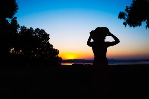 silhouette of a girl in a dress and hat at sunset in the park the girl looks at the sunset, there is a place for an inscription. High quality photo