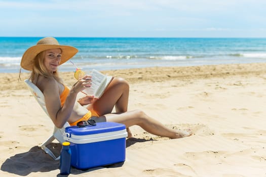 happy girl sits on the beach in a swimsuit reads a book and drinks a cocktail.beautiful seascape with a girl. High quality photo