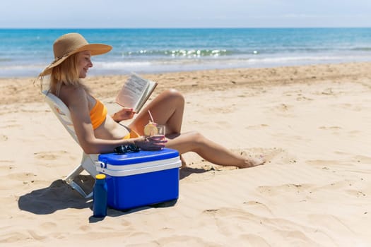 a girl of European appearance is sitting on the beach in a bathing suit reading a book and drinking a cocktail. a beautiful sea landscape with a girl. High quality photo