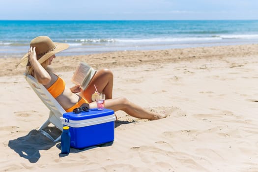 happy girl sits on the beach in a swimsuit reads a book and drinks a cocktail.beautiful seascape with a girl with a place for an inscription. High quality photo