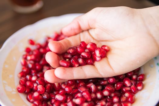 a lot of grata berries in a plate, a few red berries are held by a child's hand close-up High quality photo