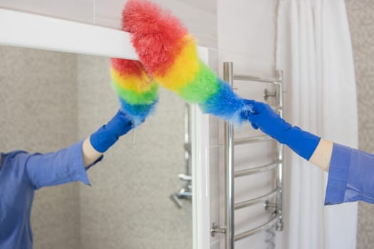 blond girl with European appearance washing mirror with colored rag in blue gloves at home.House cleaning concept