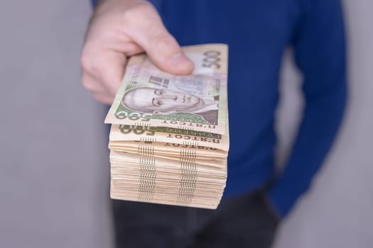 A man in a blue sweater holds a stack of new banknotes of the Ukrainian hryvnia in his hands 500 hryvnia.On a light background.500 hryvnia. High quality photo.Finance concept