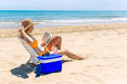 happy girl sits on the beach in a swimsuit reads a book and drinks a cocktail.beautiful seascape with a girl with a place for an inscription. High quality photo