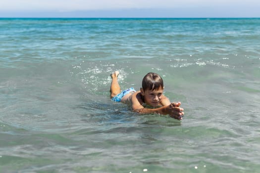 a boy of European appearance in the sea learns to swim.the concept of summer holidays.there is a place for an inscription,summer landscape with a child. High quality photo