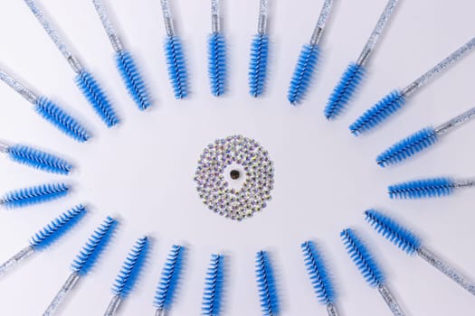 on a white background, the eye is lined with blue eyelash brushes, the pupil is lined with shiny stones inside the eye. Materials for eyelash extension. High quality photo