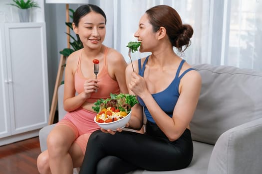 Young sporty Asian women in sportswear holding salad bowl together fill with vibrant of fruit and vegetable. Natural youthful and fit body lifestyle with balance nutrition and home exercise. Vigorous