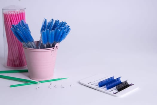 Artificial eyelashes in black and blue are glued on a white tablet on a white background. There is a for an inscription on the right.Blurred blue brushes in front of the eyelashes