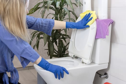 a girl of European appearance with fair hair in blue gloves is cleaning the bathroom in the house and cleans the toilet bowl with a yellow napkin