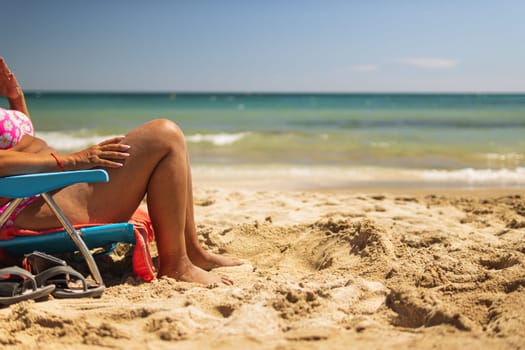 legs of a woman on the beach, a woman sunbathes on a sunbed in a sitting position on the beach, near the sea, there is a place for an inscription. The concept of summer holidays. High quality photo