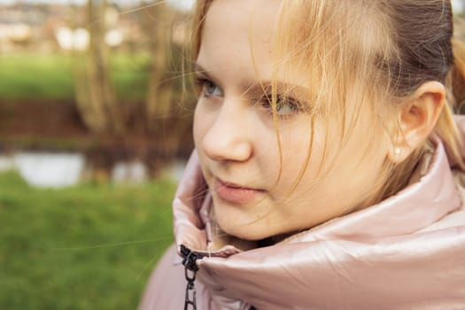 portrait of a teenage girl of European appearance with blond hair in a pink jacket in the park close-up, the child looks to the side. High quality photo