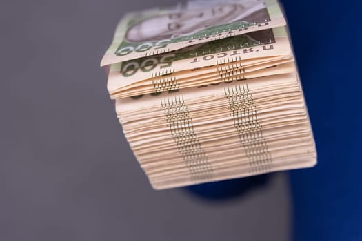 A man in a blue sweater holds a stack of new banknotes of the Ukrainian hryvnia in his hands 500 hryvnia close-up.On a Gray background.500 hryvnia close-up. High quality photo.Finance concept