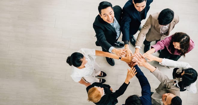 An overhead shot captures four diverse business colleagues in a unity circle stacking their hands. This symbolizes teamwork success and global cooperation in the corporate world.