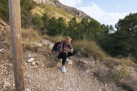 a girl in sportswear sits on a stone, rests from a hike in the mountains, a girl sits looking at the phone. High quality photo