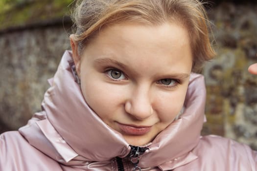 portrait of a teenager girl of European appearance with blond hair in a pink jacket, close-up, the child makes different emotions. High quality photo