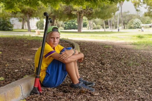 teenager in casual clothes sitting in the park on a scooter relaxing, active lifestyle of a child. High quality photo