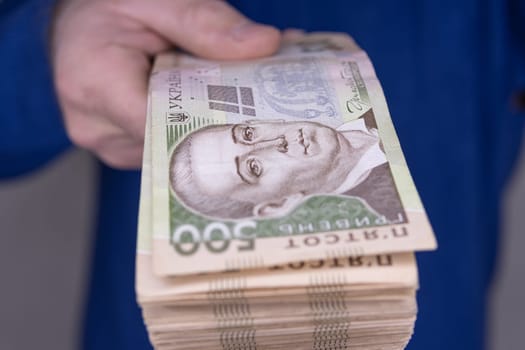 A man in a blue sweater holds a stack of new banknotes of the Ukrainian hryvnia in his hands 500 hryvnia close-up.On a light background.500 hryvnia close-up. High quality photo.Finance concept