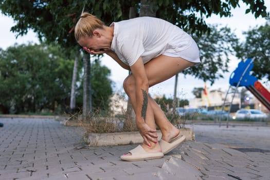 a girl of European appearance in shorts and a T-shirt, standing on the street holding her leg and screaming in pain, the girl tripped over an old paving slab. insurance case concept.High quality photo