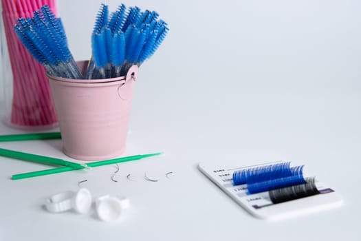 Artificial eyelashes in black and blue are glued on a white tablet on a white background. There is a for an inscription on the right.Blurred blue brushes in front of the eyelashes