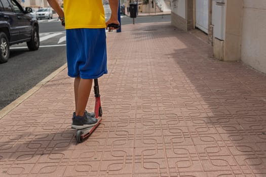 a child in casual clothes rides a scooter on the street, with his back turned to the camera, there is a place for an inscription. High quality photo