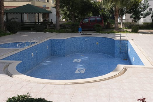 new pool without water in the hotel in the backyard, tiled, green trees and grass around. High quality photo