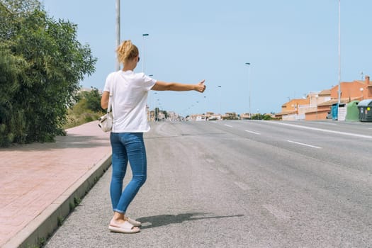 a girl in casual clothes stands on the road with her back to the camera and stops the car on the road, there is a place for an inscription. High quality photo