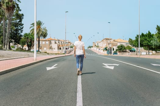 a european girl in a t-shirt and jeans walks along the road with her back to the camera, a beautiful cityscape with a girl. High quality photo