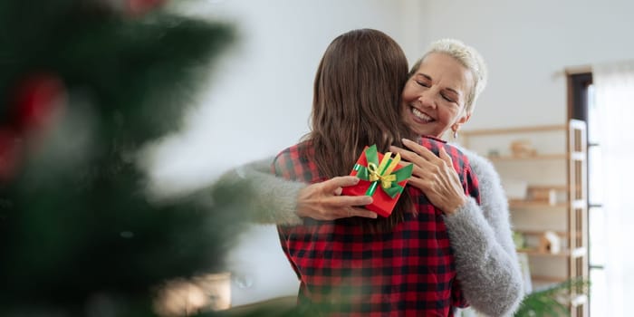 Thankful Caucasian woman with christmas gift hugging daughter at home.