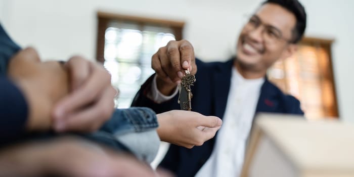 Happy real state agent giving new house key to a young couple. Real estate concept.
