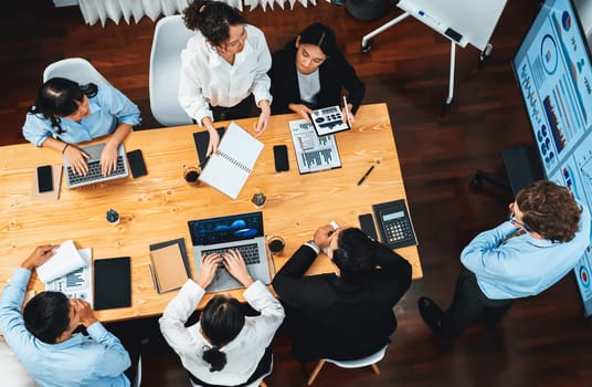 Wide top view of diverse group of business analyst team analyzing financial data report paper on meeting table. Chart and graph dashboard by business intelligence analysis. Meticulous