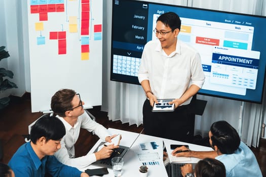 Project manager communicate and collaborate with team using project management software display on monitor, tracking progress of project task and making schedule plan at meeting table. Prudent