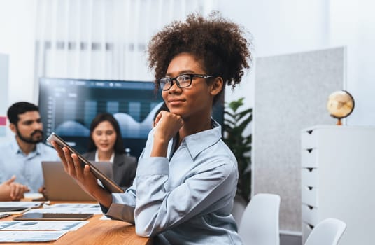 Happy young african businesswoman wearing glasses portrait with group of office worker on meeting with screen display business dashboard in background. Confident office lady at team meeting. Concord