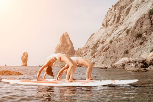 Woman sup yoga. Middle age sporty woman practising yoga pilates on paddle sup surfboard. Female stretching doing workout on sea water. Modern individual hipster outdoor summer sport activity