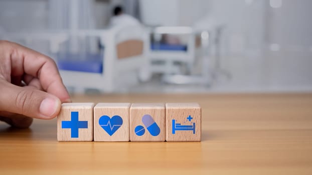 Health and medical concept Human hand holds a wooden block with icons about health and access to treatment and medicine and supplies on a blue background.