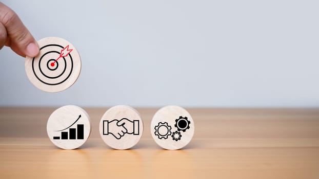 Businessman's hands hold a circular wooden board with printed target icons, business goals and objectives concept, business competition.