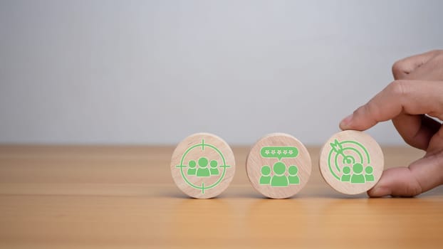 Human hands hold target customer icons on circle wooden planks. Placed on a wooden background, it represents selected business goals, target customers, marketing plans and strategies including customer-centric strategies.