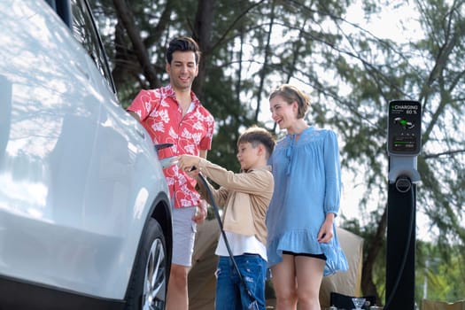 Outdoor adventure and family vacation camping in nature travel by eco friendly car for sustainable future. Lovely family recharge EV car with EV charging station in campsite. Perpetual