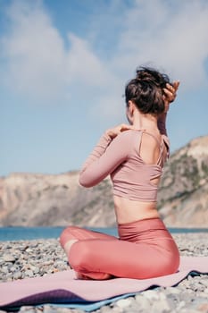 Young woman with long hair in white swimsuit and boho style braclets practicing outdoors on yoga mat by the sea on a sunset. Women's yoga fitness routine. Healthy lifestyle, harmony and meditation