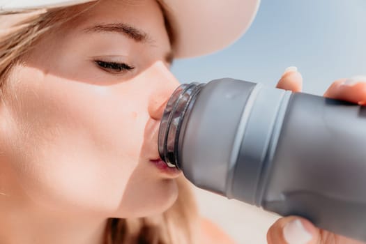 Fintess woman drinking water. Happy, active middle aged woman standing on beach and drinking water after excersise. Concept of lifestyle, sport. Close up.