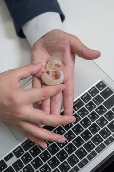 Close-up of a man's hands with a hearing aid near a laptop. Vertical photo